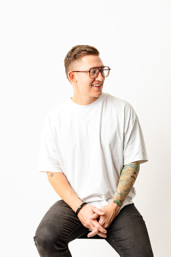 Man in glasses looks off to side on a white backdrop.