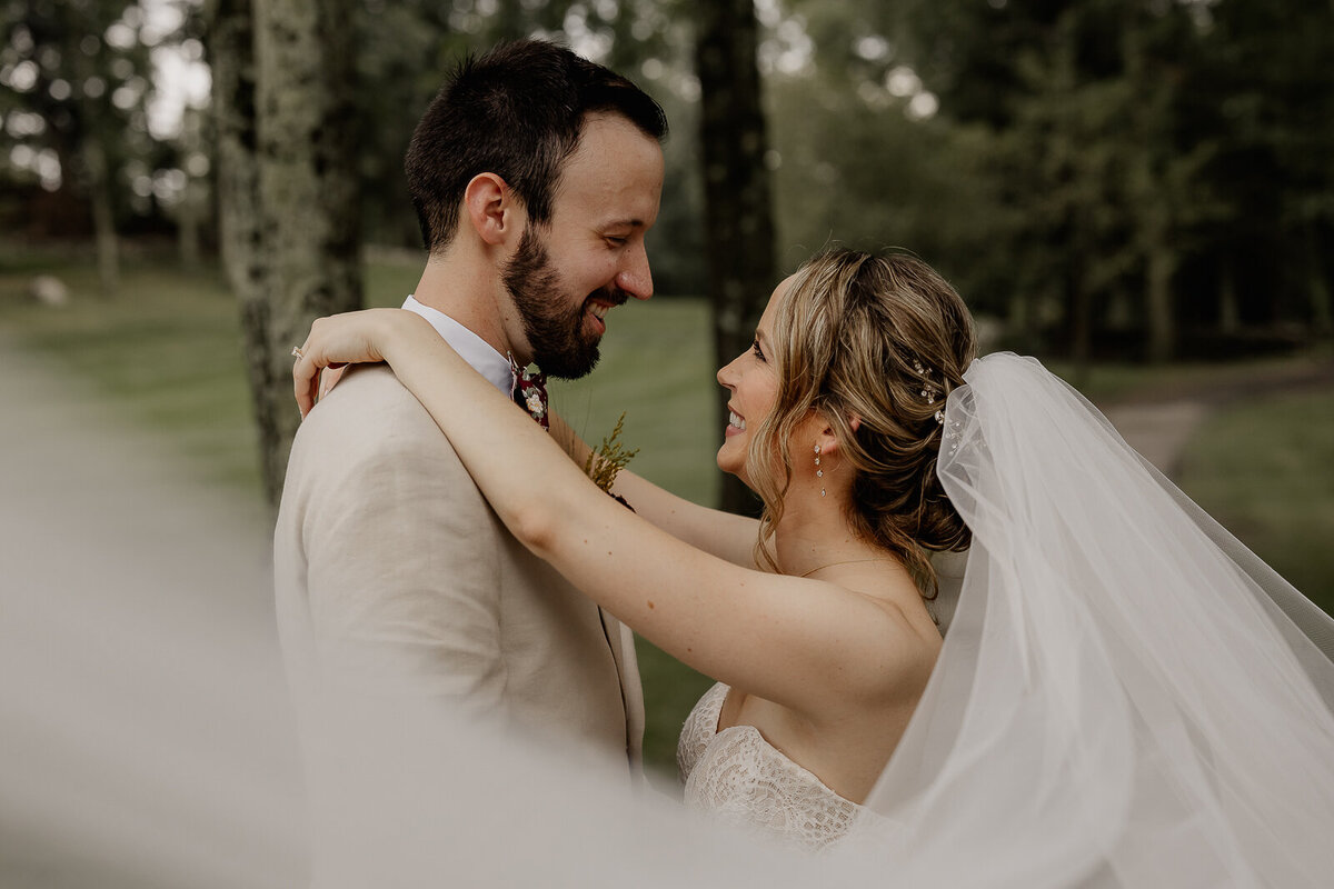 New York bride and groom stand under a tree smiling at one another