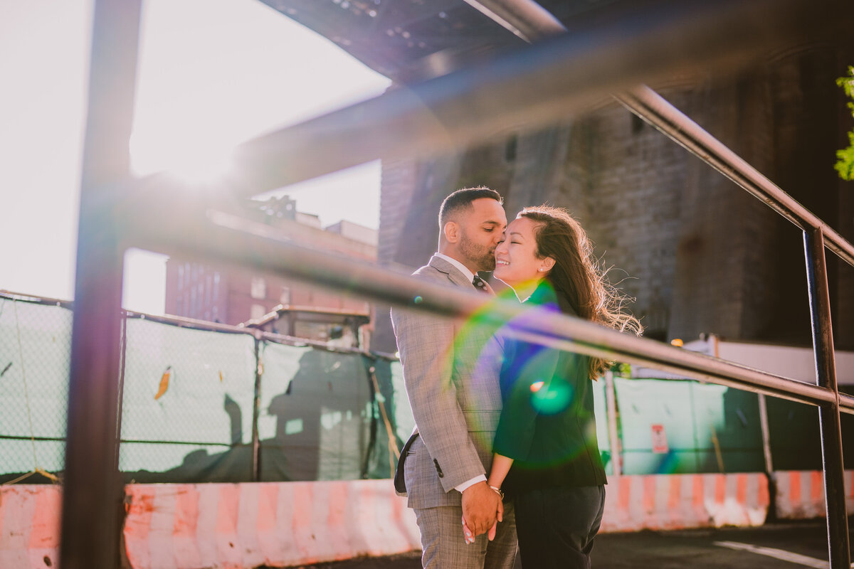 Groom kiss bride on the cheek during their engagement session in brooklyn dumbo