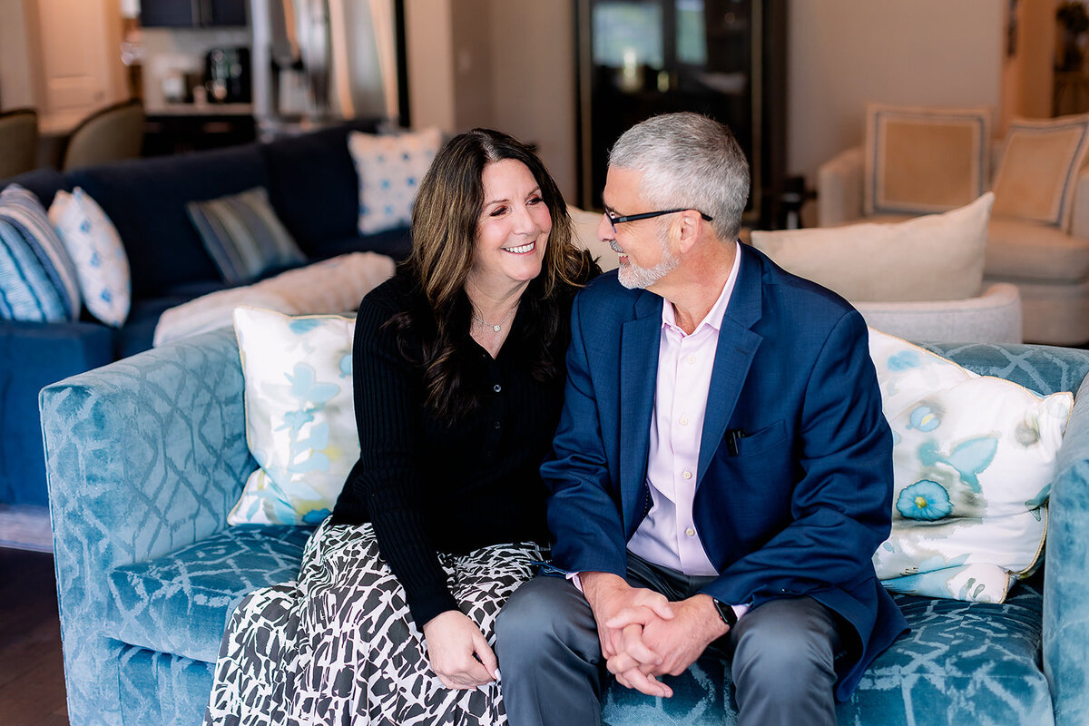 Owners of Arciera Home Care smiling and looking at each other on a blue couch