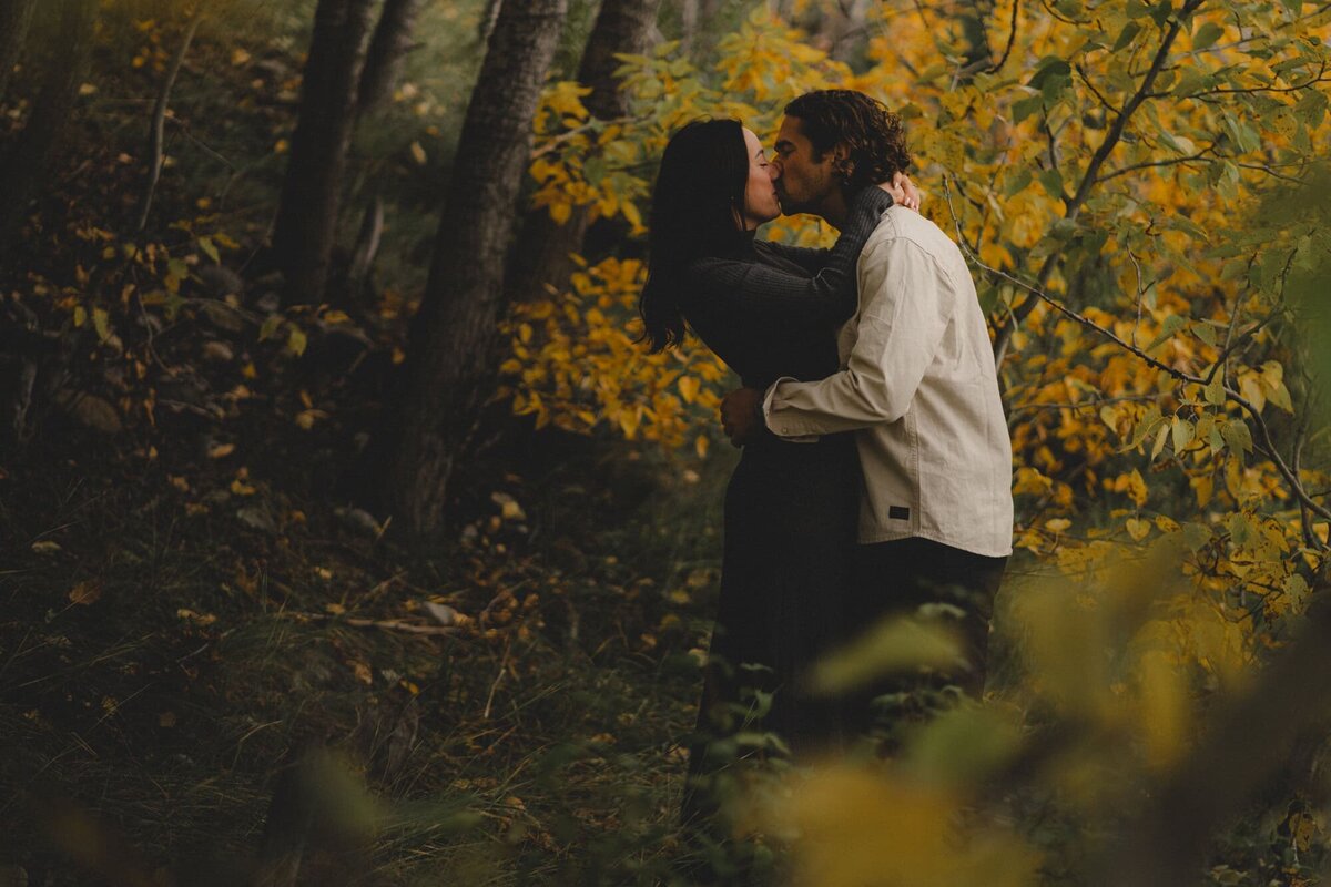 Engaged couple kissing in front of fall colours in Banff