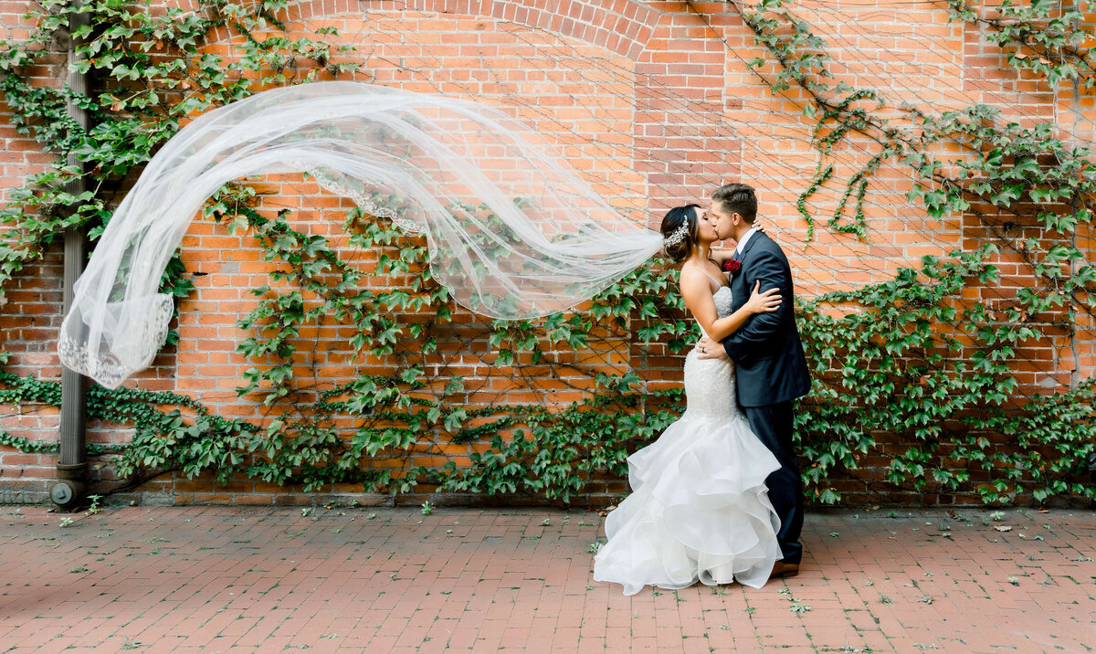 A bride and groom kissing and the veil flowing in the wind