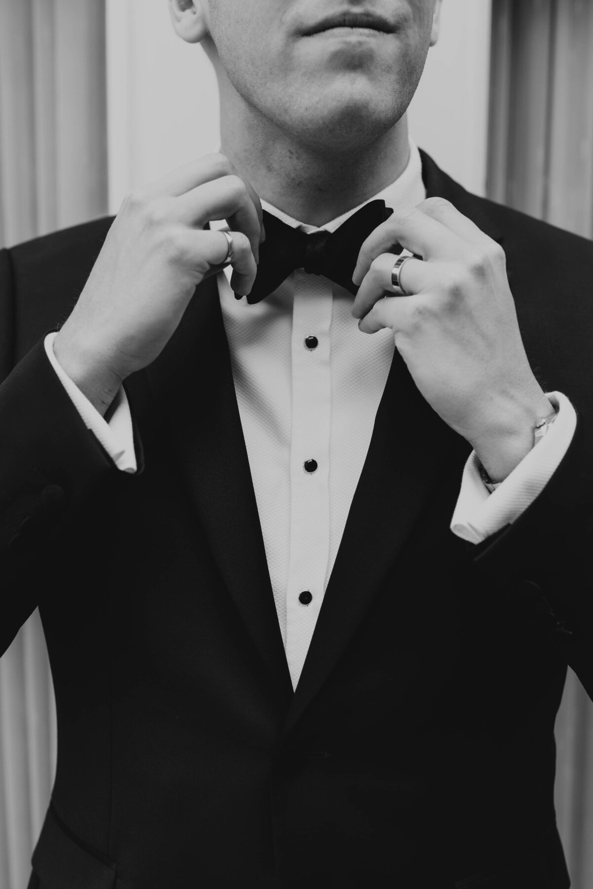 Groom adjust his bow tie in black and white portrait.
