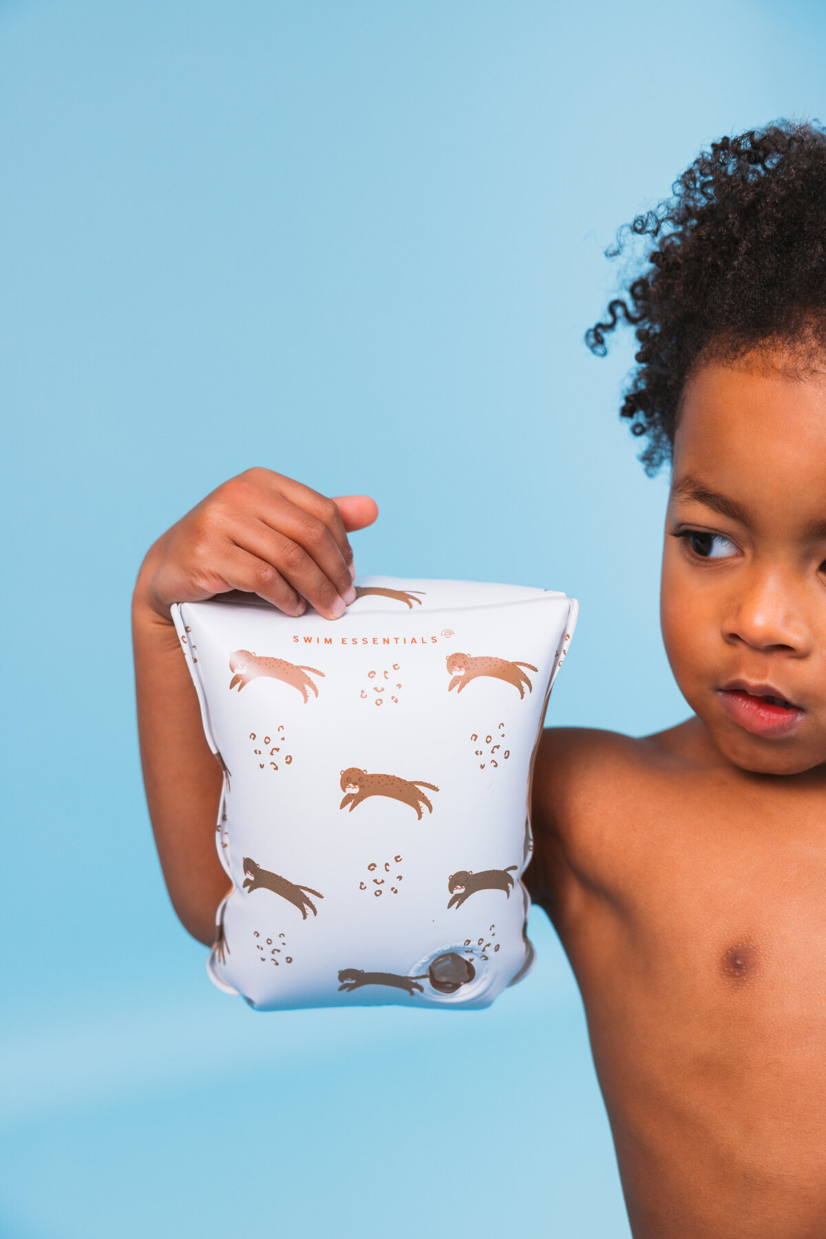 Child holding up a Swim Essentials armband with playful otter print, set against a bright blue background.