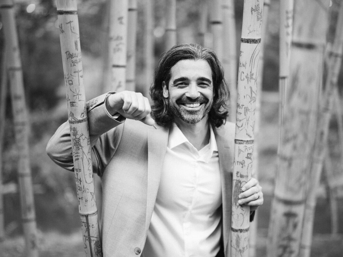 A man smiling and leaning on skinny trees.