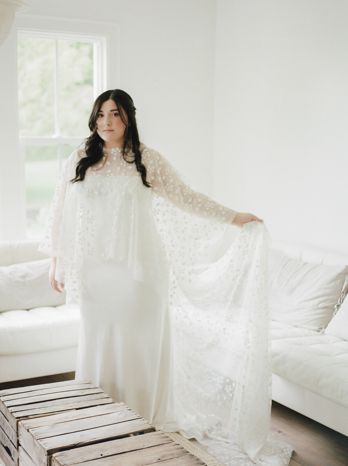 Bride adjusts bridal cape in white getting ready room at Glass House Community, west Michigan wedding venue