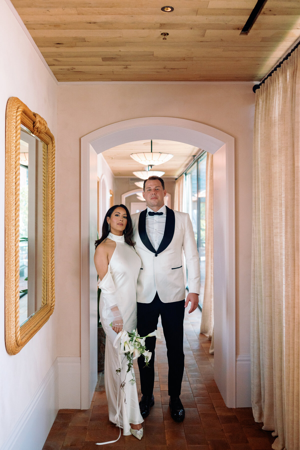 Bride and groom pose hand in hand in an elegant hallway with arched doorways during their New York City elopement.