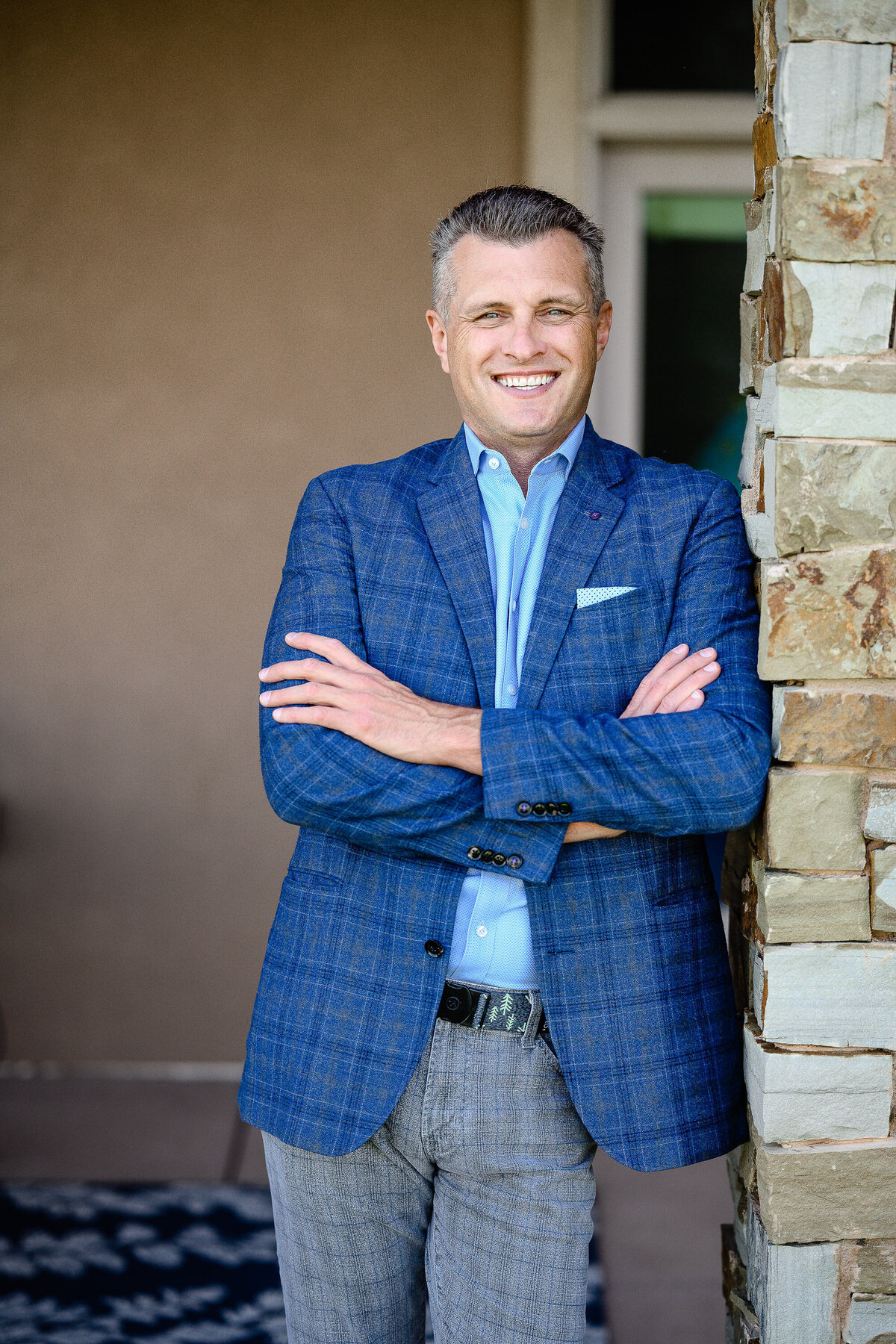 A brand photographer in Denver takes pictures of a business man in a blue plaid suit leaning on a wall for his brand pictures and branding photos.