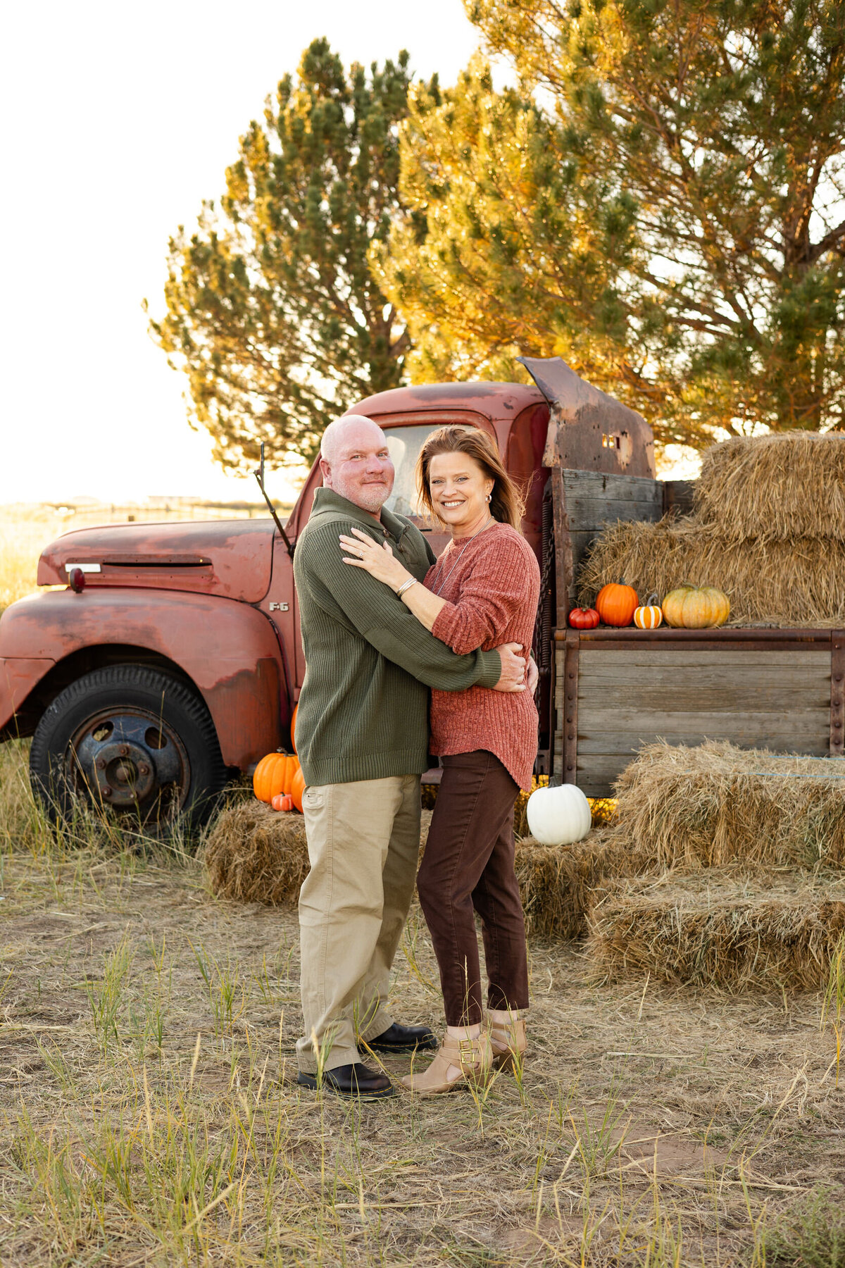 Husband and wife stand in front of vintage red farm truck and smile at the camera.