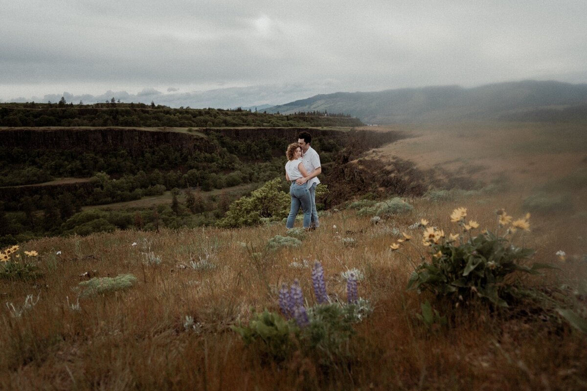 A couples portrait of a male and female embracing in wildflower field at Rowena Crest Viewpoint near Hood, Oregon