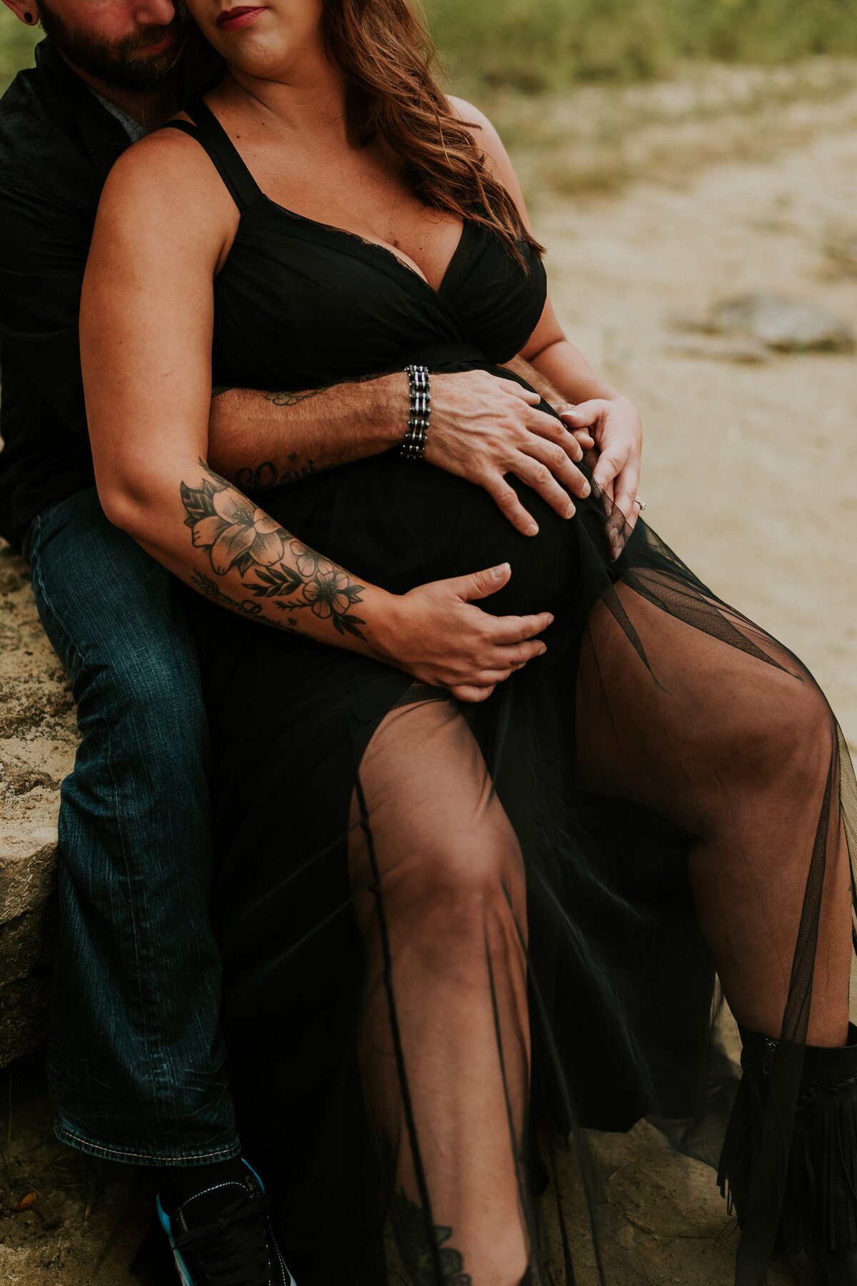 Stillwater couple holding maternity belly while sitting on a rock in Stillwater by the river
