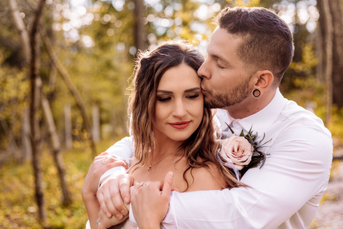 Groom kisses brides temple as he embraces her