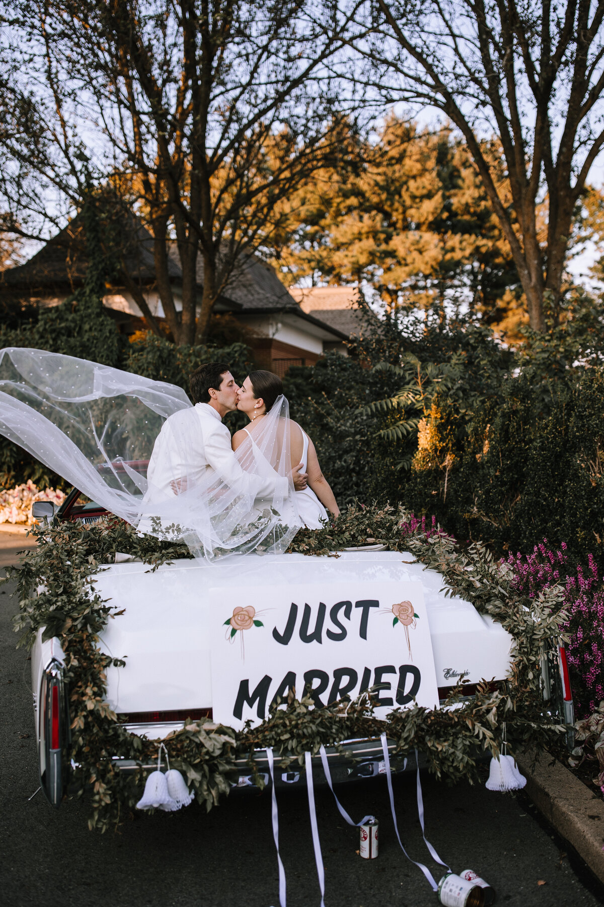Bride and groom kissing on the back of a vintage car.