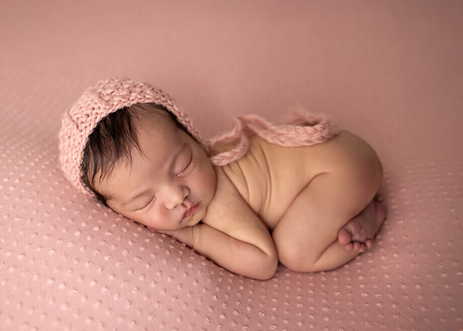 baby girl bum up on a textured pink backdrop with a matching bonnet
