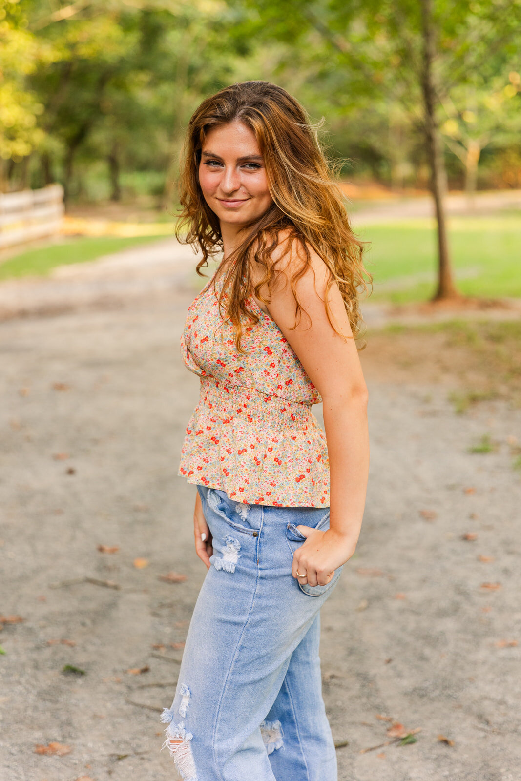 High school senior girl wearing jeans and sleeves less top standing on a park path during summer photo session with Laure Photography