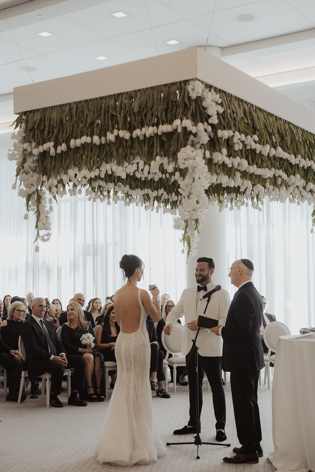 A bride and groom stand under a suspended chuppah of floating white tulips at the Four Seasons.