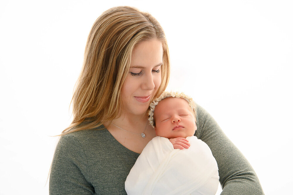 mom holding her newborn girl wrapped in white.