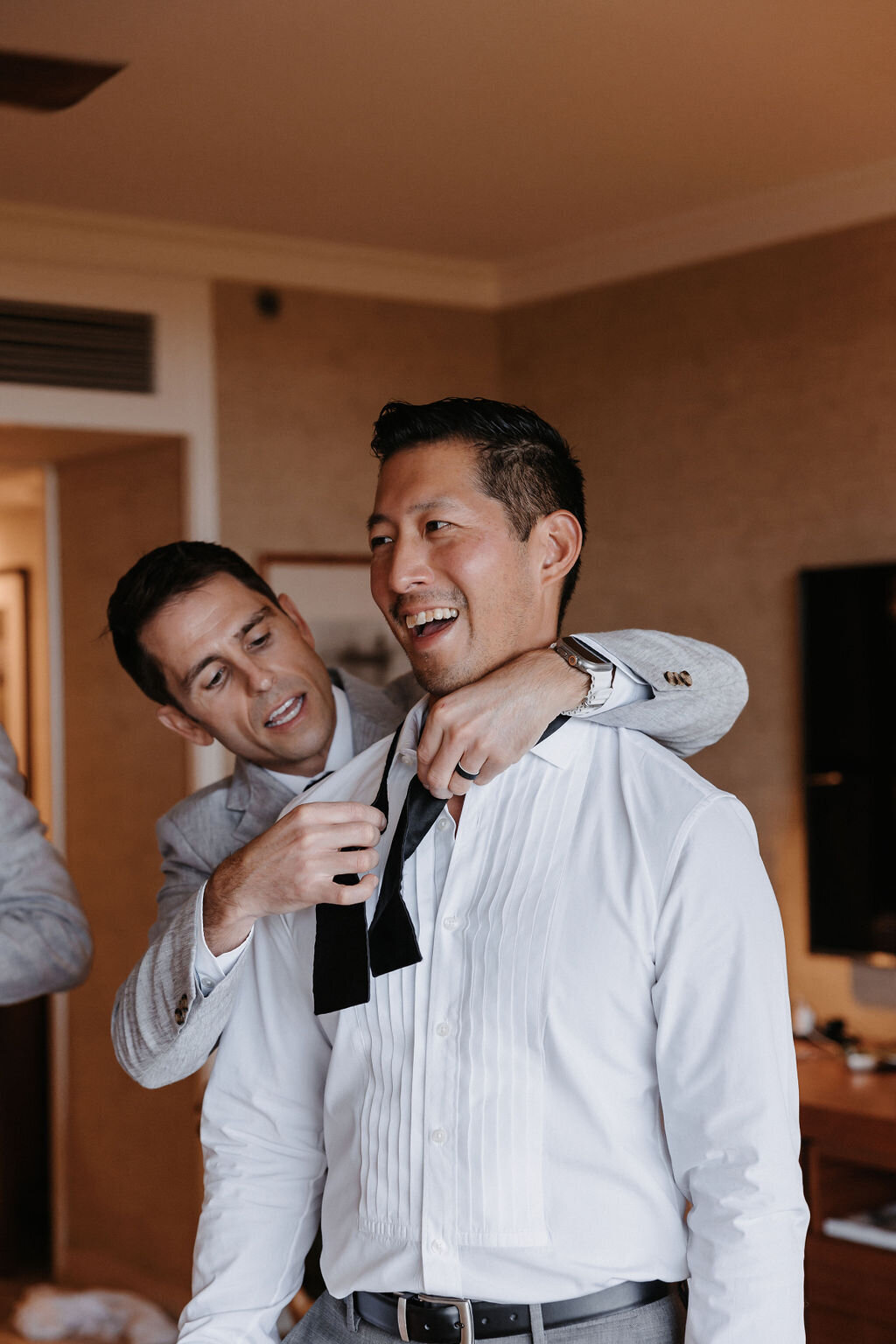 groom having bowtie tied from groomsman standing behind him at four seasons oahu hotel room