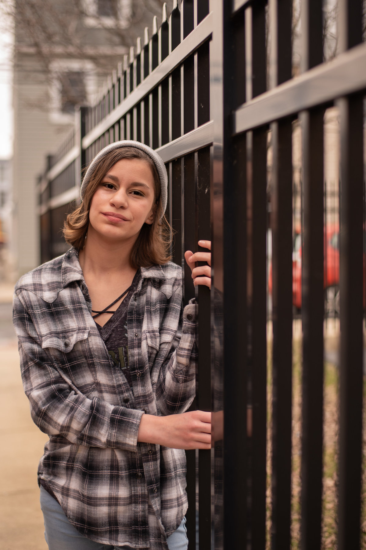 Teen Girl in gray flannel shirt and cap posed along black metal fence