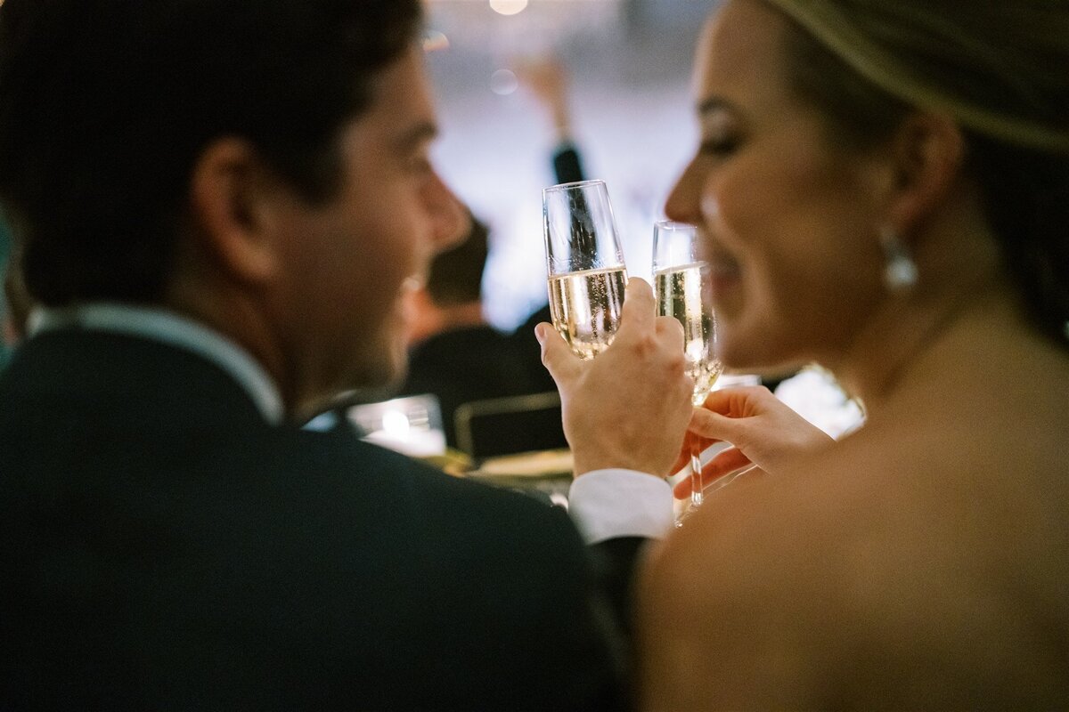 A close up of the bride and groom at the table holding Champagne. 