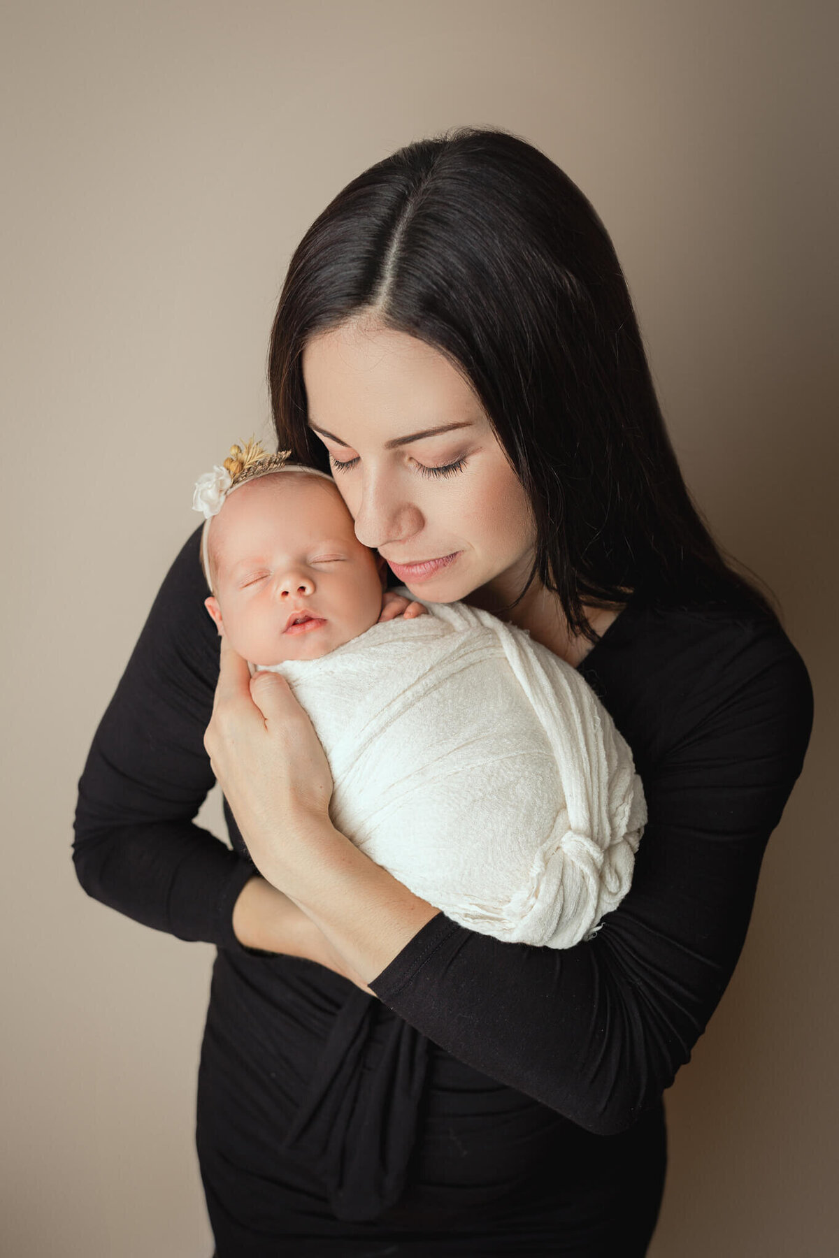 proud mother snuggling in close to her newborn baby girl on beige backdrop, hamilton, ON newborn studio