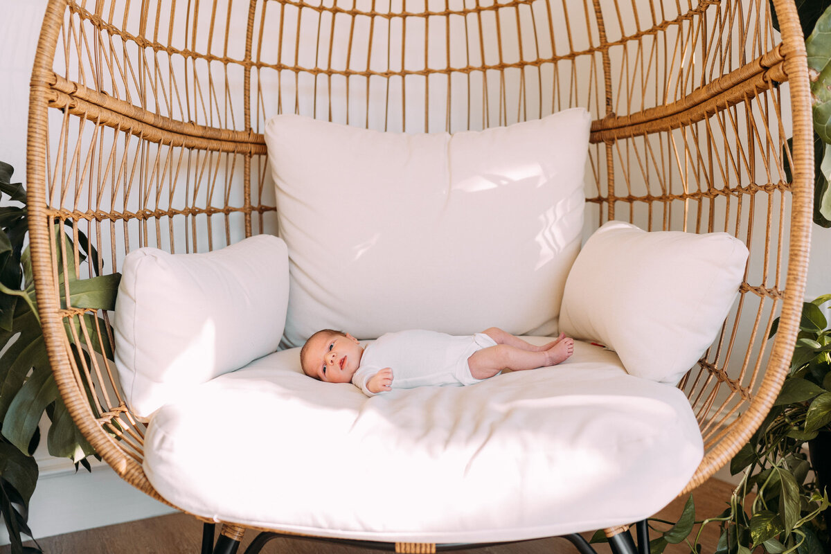 infant baby lies in circle chair wearing white onesie