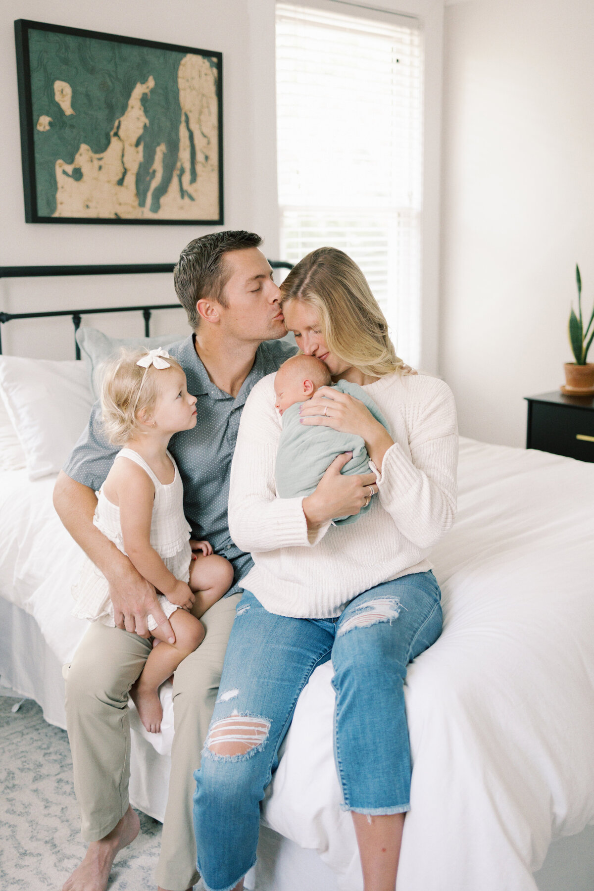 Dad holding toddler sister but mom is cuddling newborn baby and kissing his head in Williamsburg Virginia