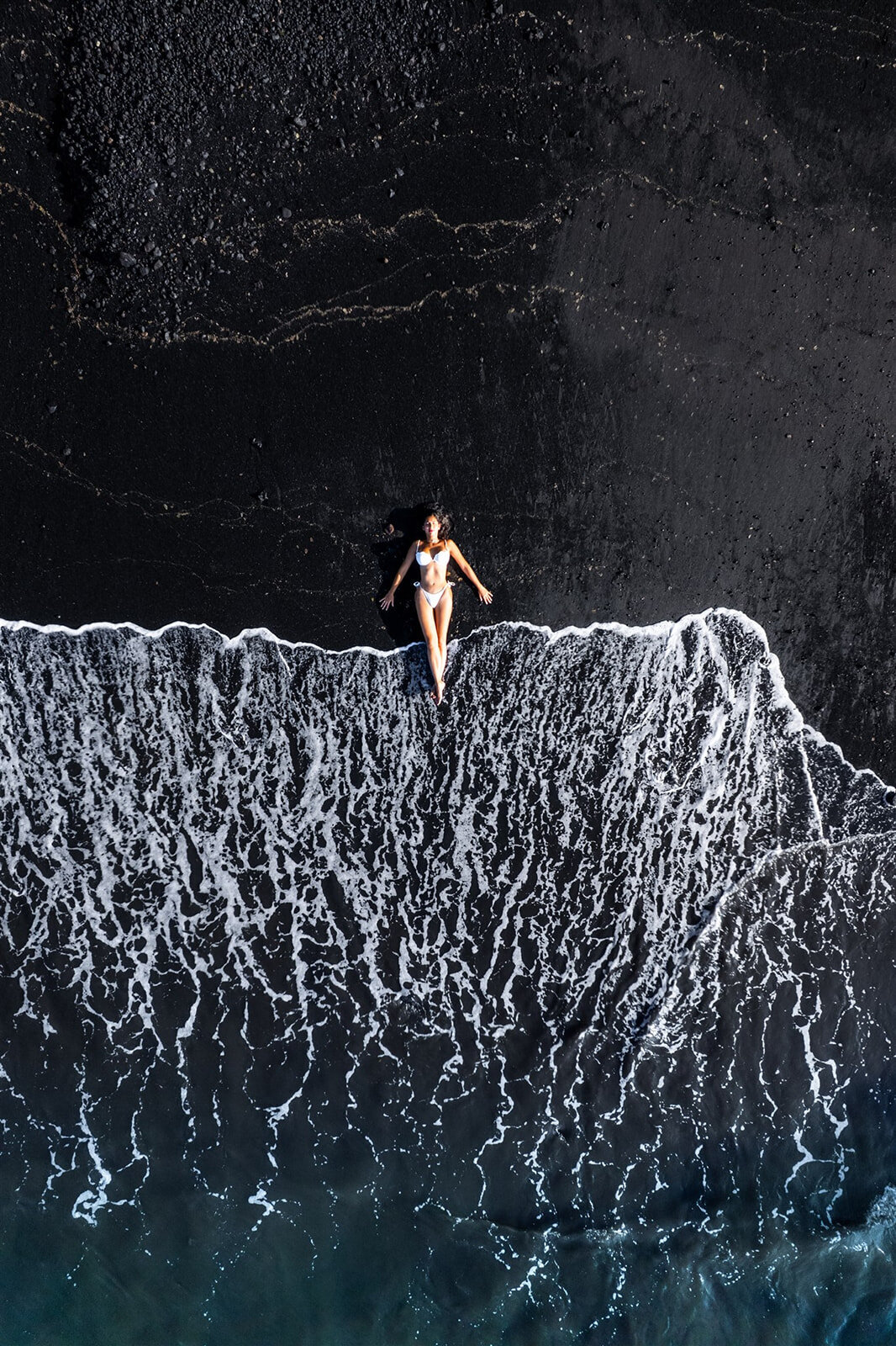 Drone photo of woman laying on black sand beach, posing for individual portrait photographer Hawaii Adventure Portraits
