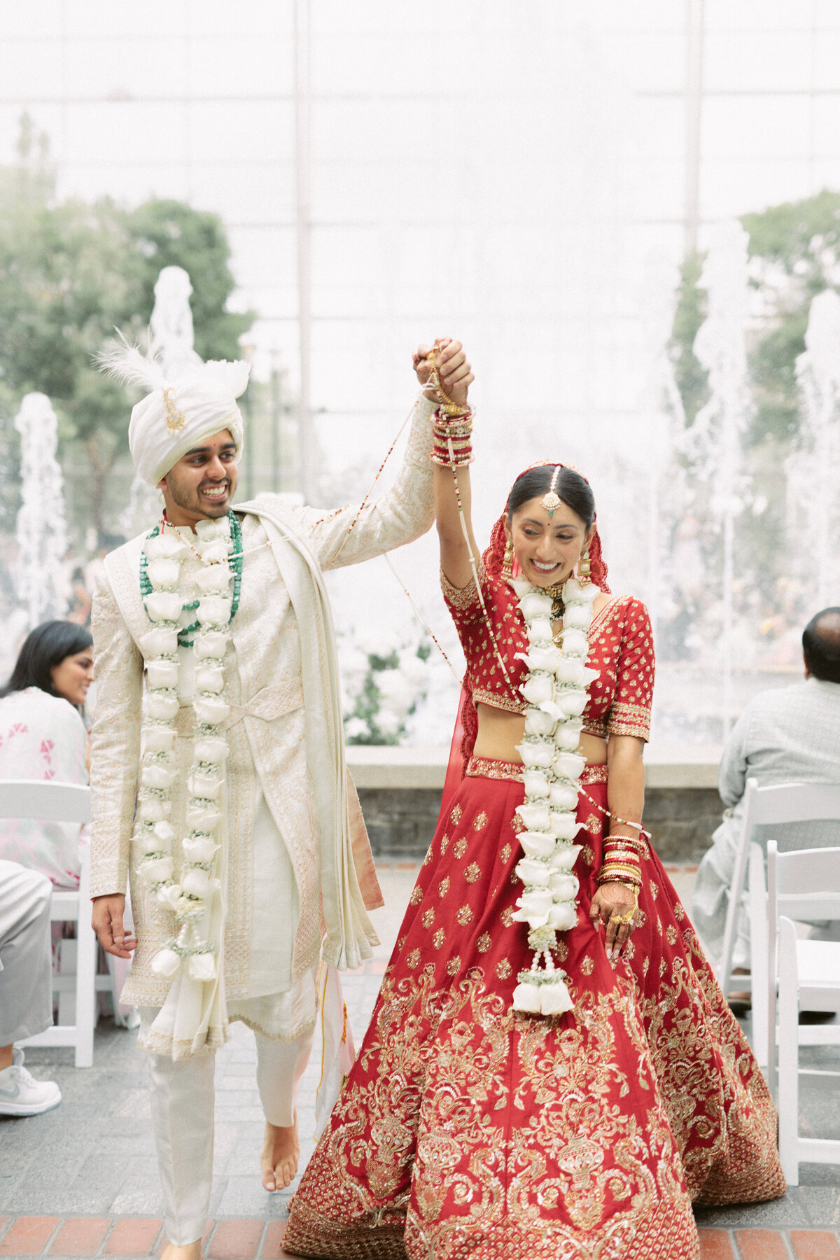 Bride and groom walking joyfully down the aisle after their Hindu ceremony, adorned with floral garlands.