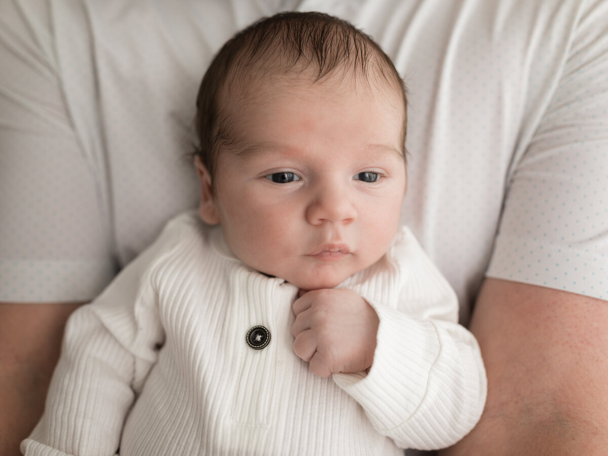 dad holding newborn baby boy in white onesie for studio photoshoot 
