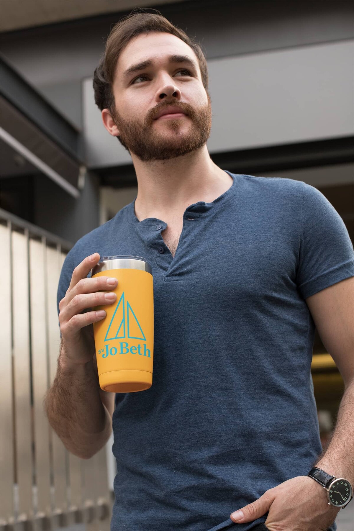A pensive, bearded man holds an orange travel mug with a blue SV Jo Beth logo