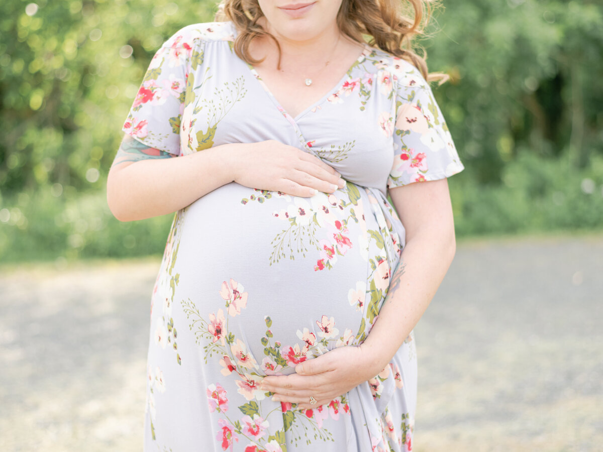 Mom in floral dress holding her belly with both hands during Richmond VA maternity session.