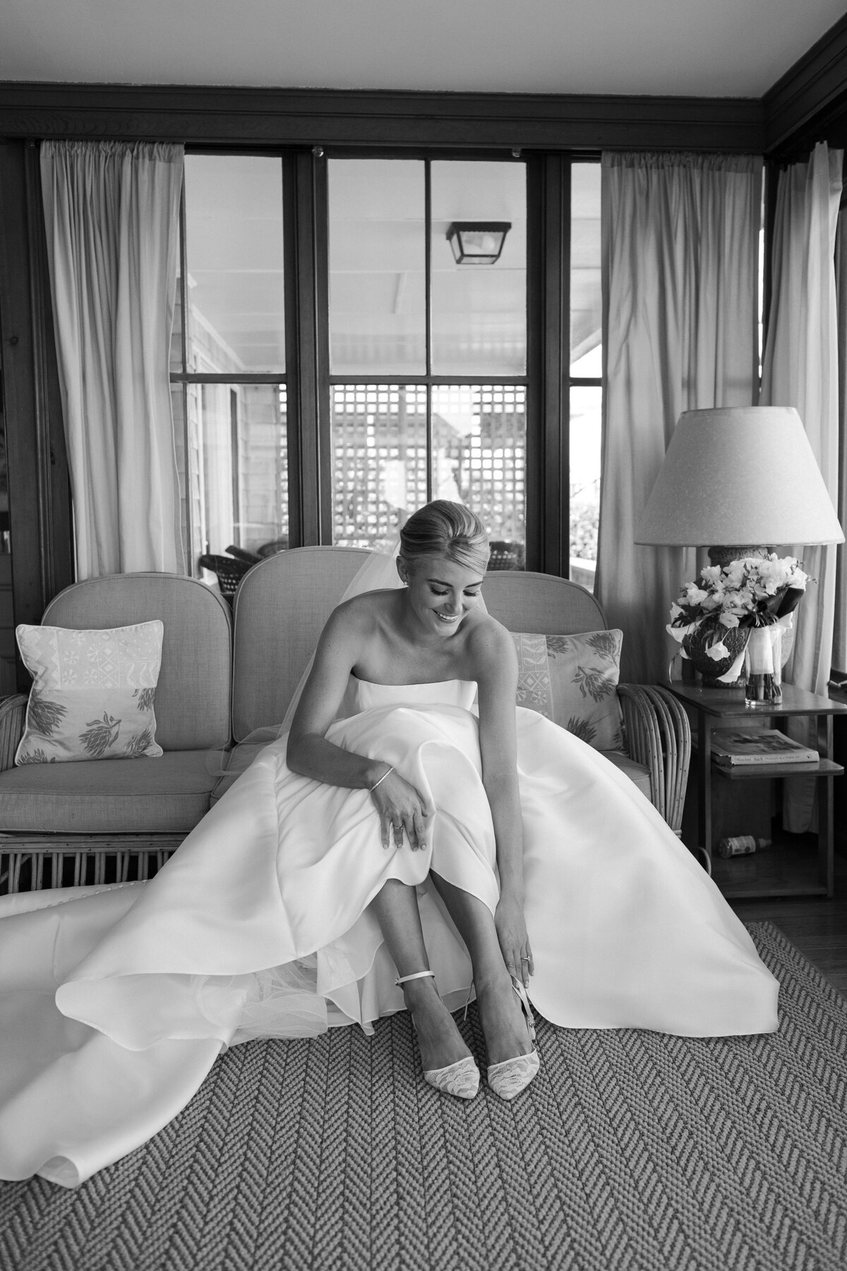 Bride sits in wedding gown as she adjusts her shoe on wedding day.