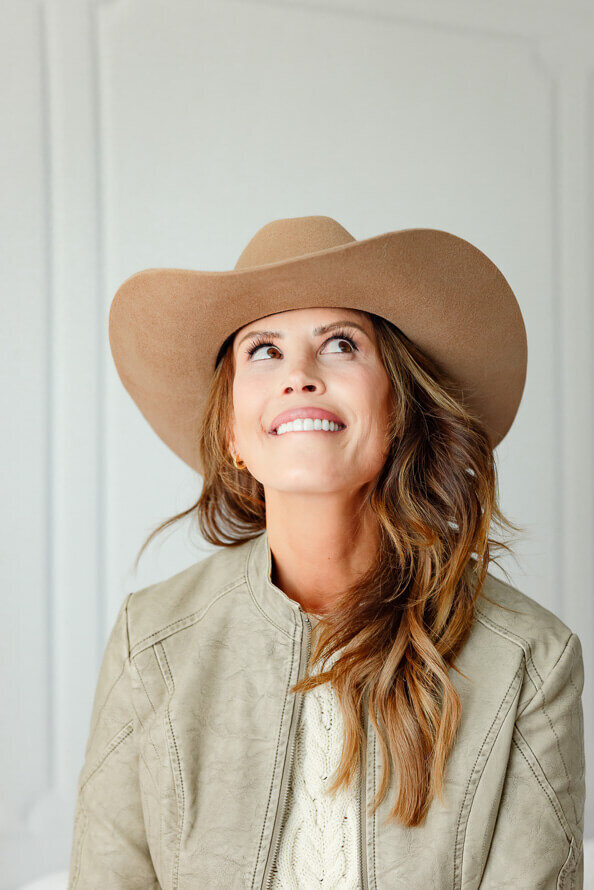 Girl in cowgirl hat bites lip and look upward in a light photography studio.
