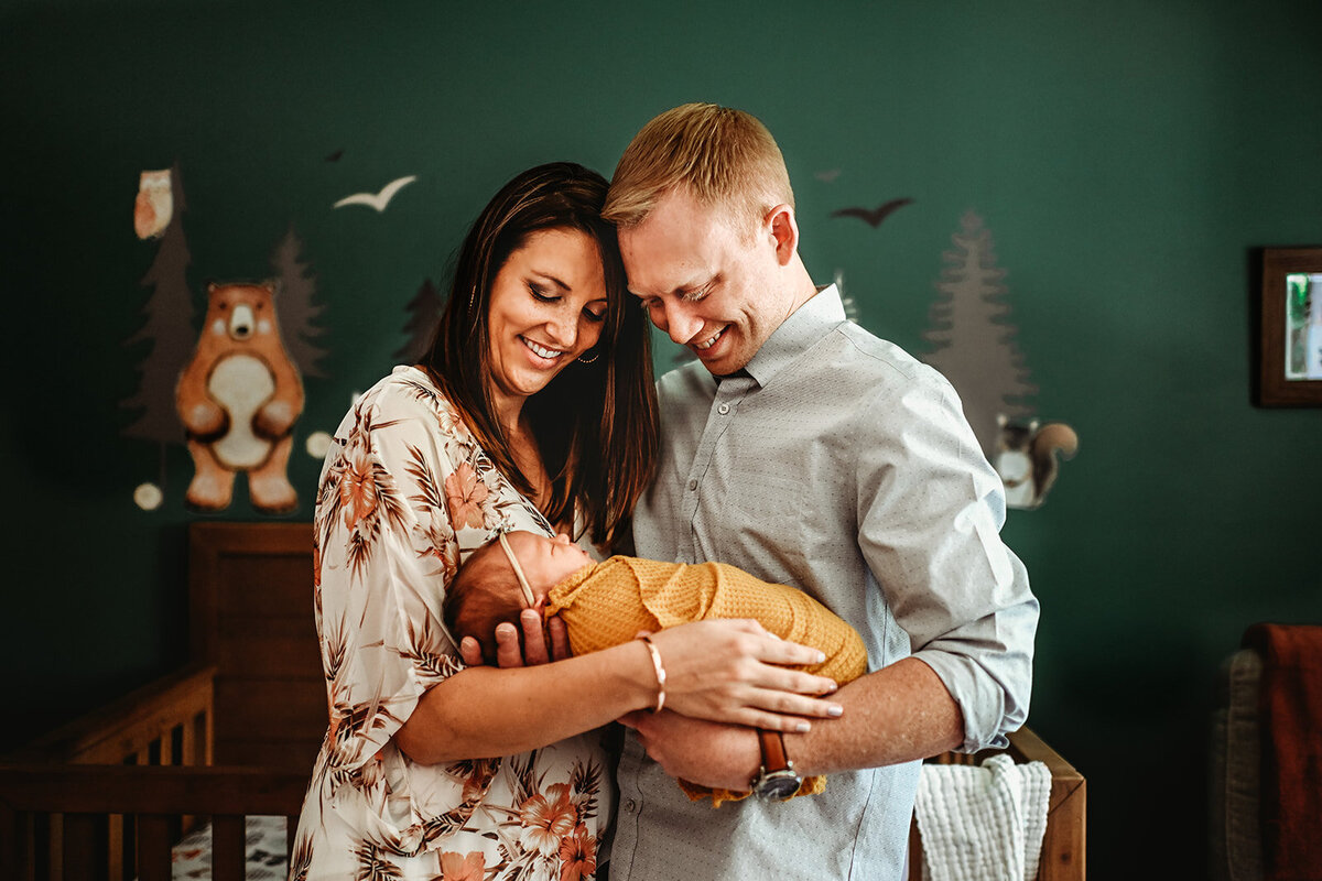 in home photo session for a newborn photo shoot with mother and father holding their newborn baby in his emerald green nursery captured by Family photographers Maryland