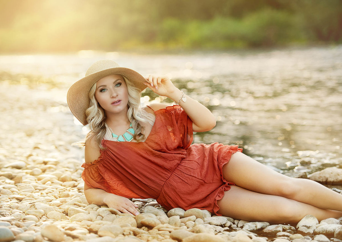 girl in orange romper and sun hat laying on beach for senior outdoor photos