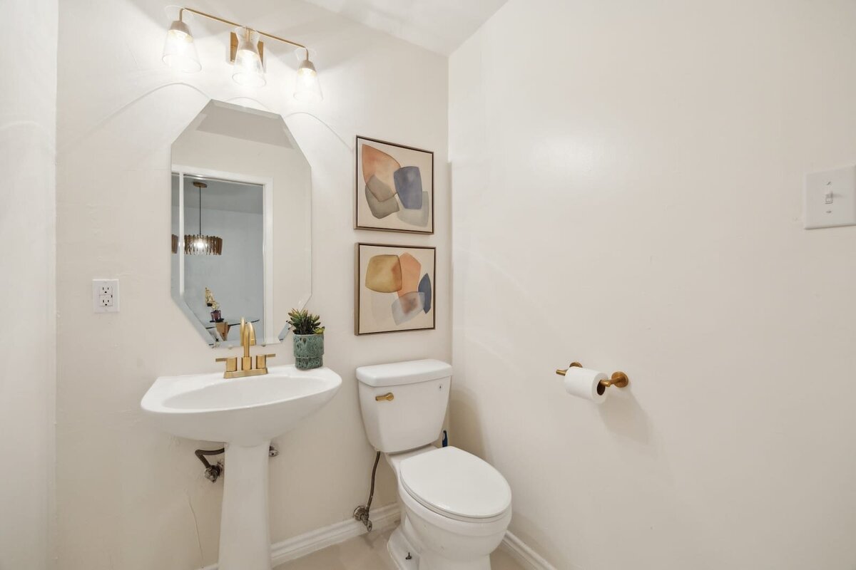 Powder bathroom at 3120 Chapel Downs Dr Dallas TX showcasing pedestal sink, gold faucet, modern lighting, and minimalist decor — listed by Haven Realty Group.