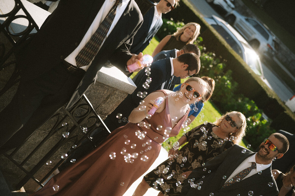 A wedding guest using a bubble machine and smiling 