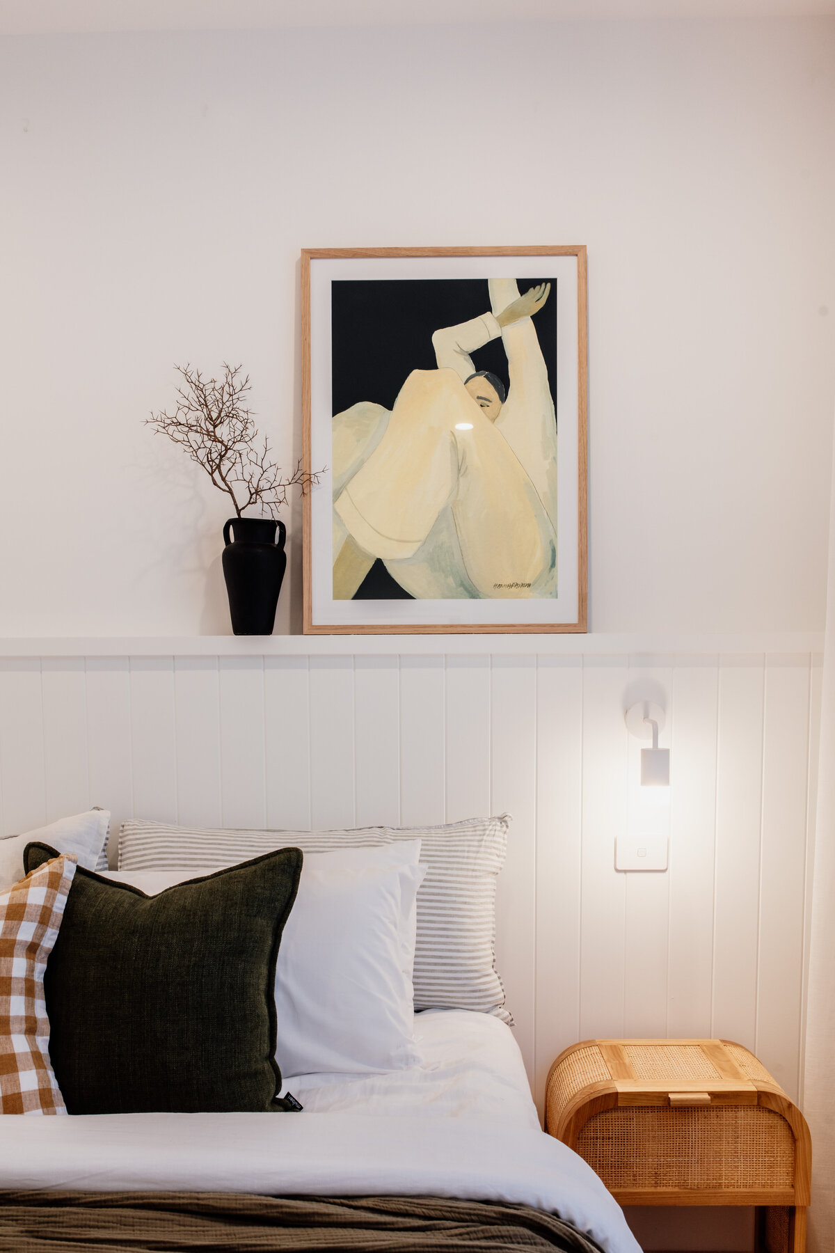Cozy bedroom with art piece above bed, pillows, and side table with vase. Soft lighting creates a warm atmosphere, crafted by a Full-Service Interior Design Newcastle expert.