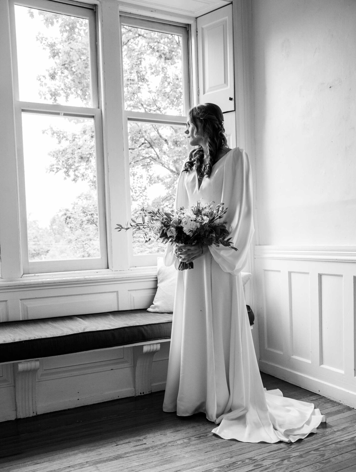 Black and white image of Bride standing in front of window holding bouquet