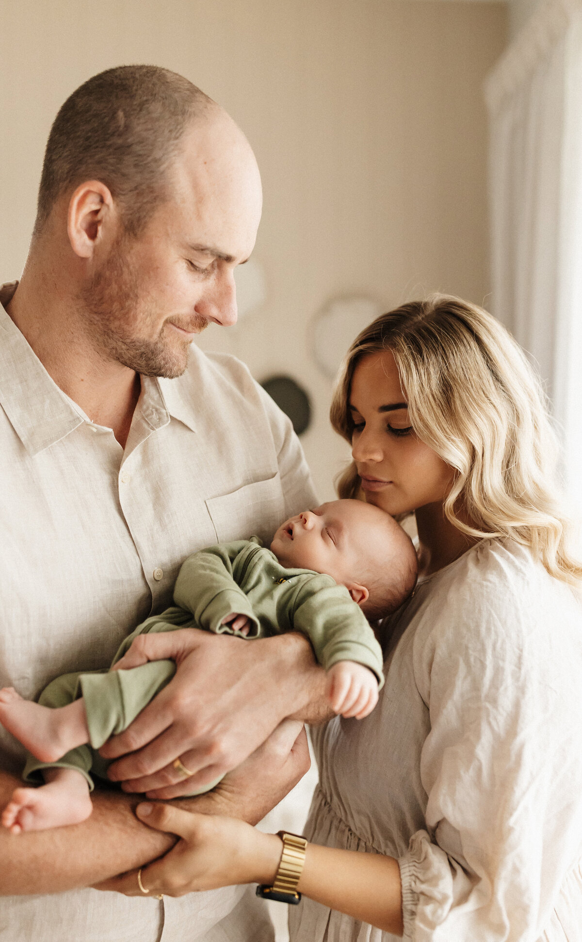 A mother and father holding their newborn baby wearing creams and green during a family in home newborn photoshoot in christchurch