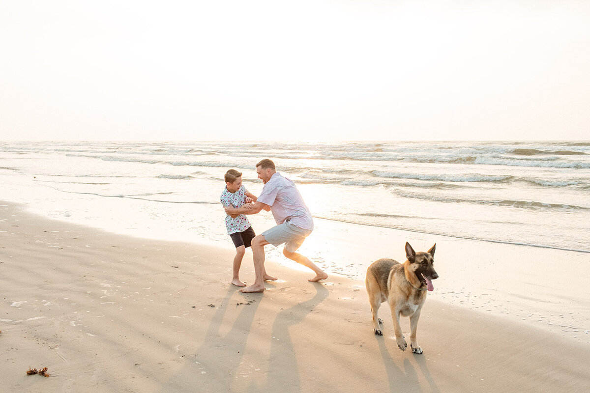 Parent with child and dog enjoying beach time in golden sunlight - Sara James creates memorable coastal family portraits including beloved pets during seaside photography adventures in Texas Gulf Coast locations