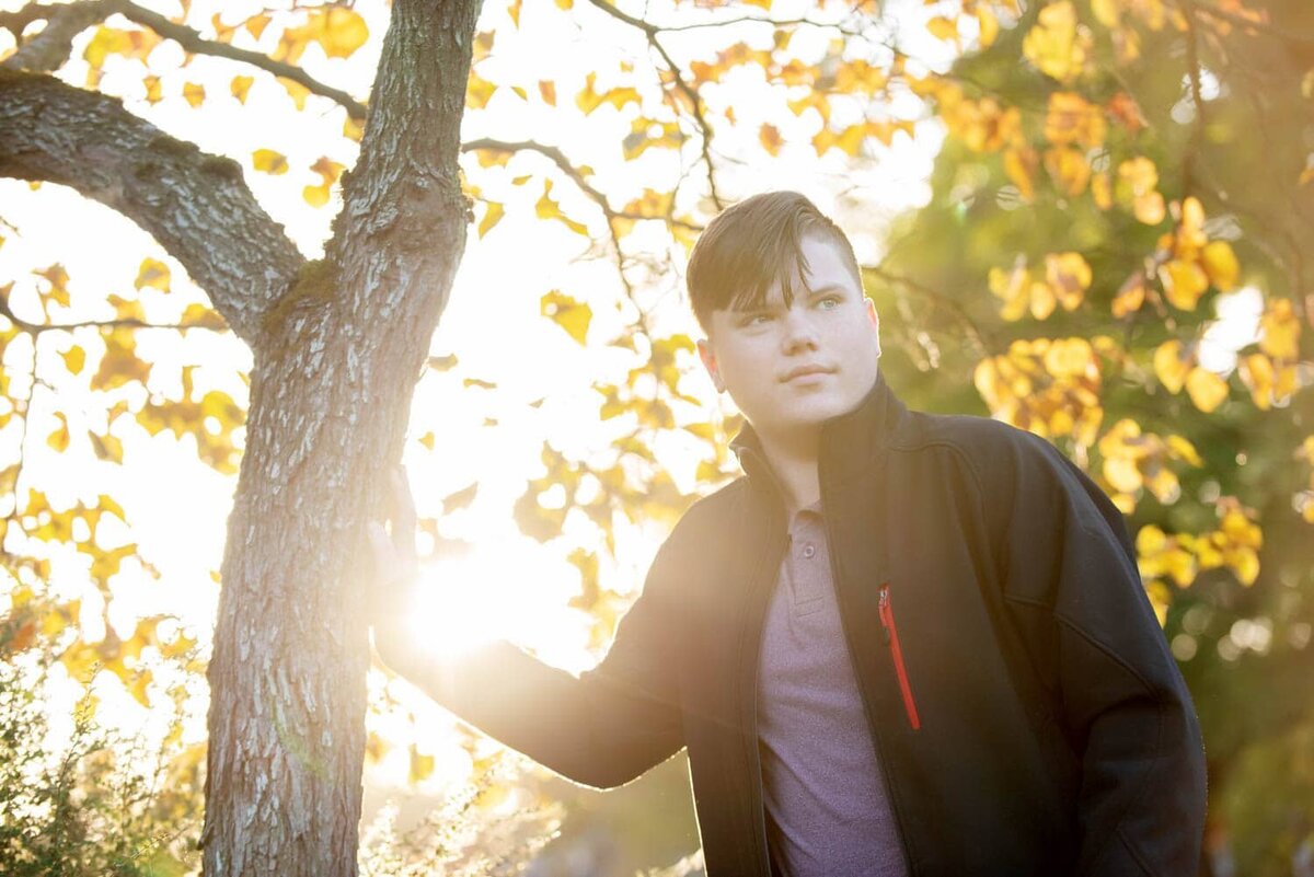 Casual fall sunset senior photograph of young man next to a yellow tree.
