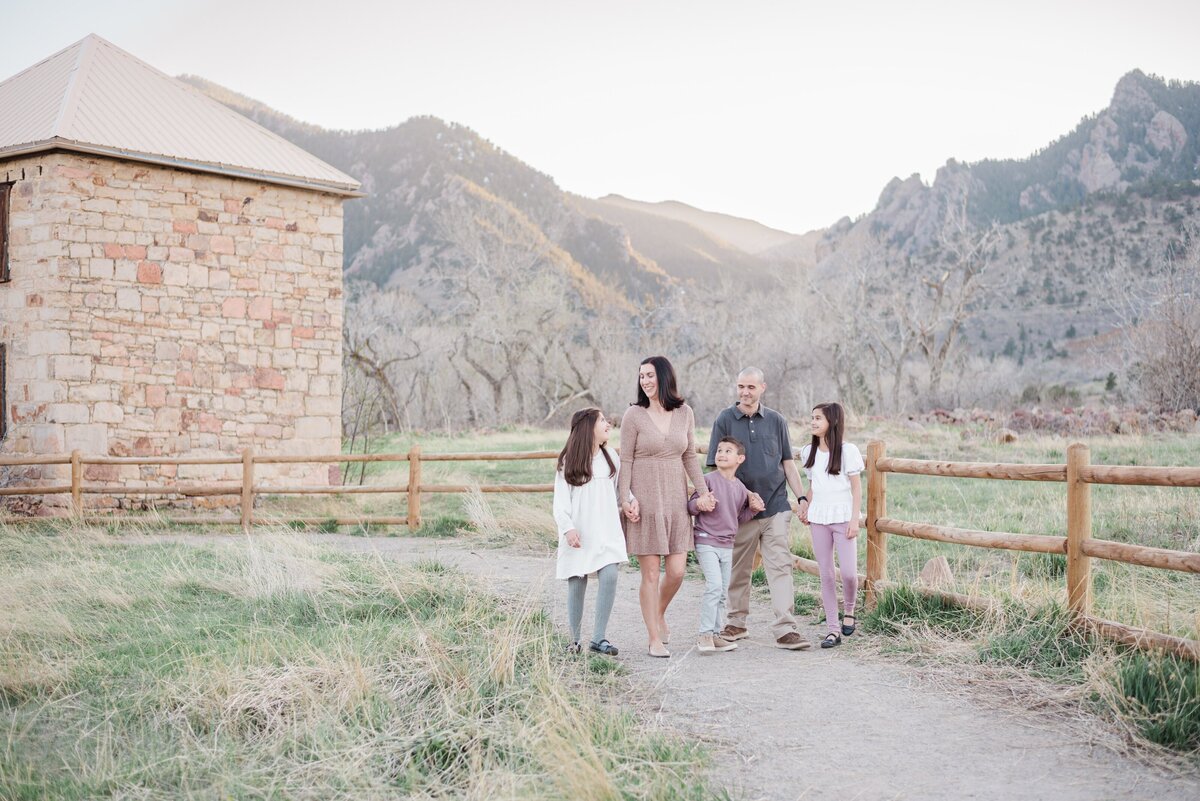 Daughter, mom, don, dad, and another daughter all hold hands and walk in a line along a path near a wooden fence at South Mesa Trailhead