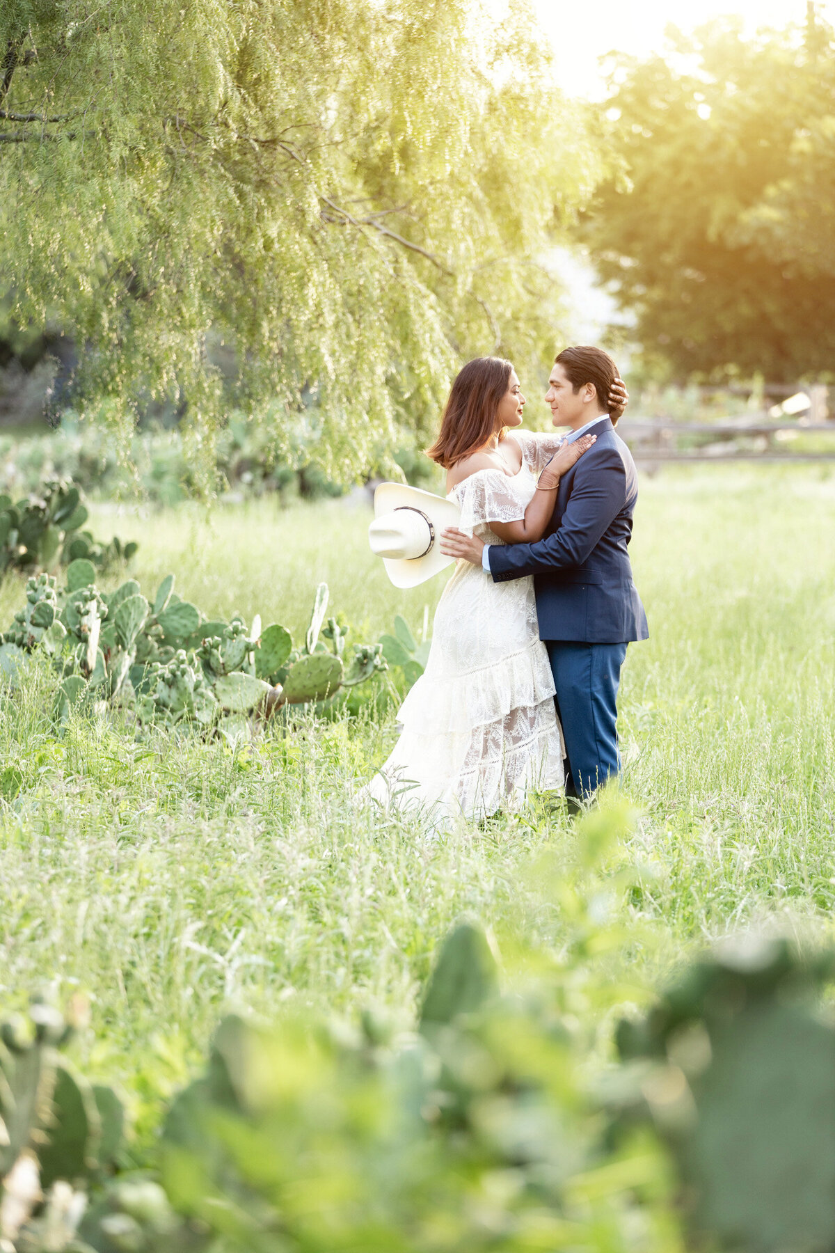 Engaged couple at sunset during a country-style engagement session at the Drover Hotel in Fort Worth, posing in a field with cactus plants and wearing cowboy hats