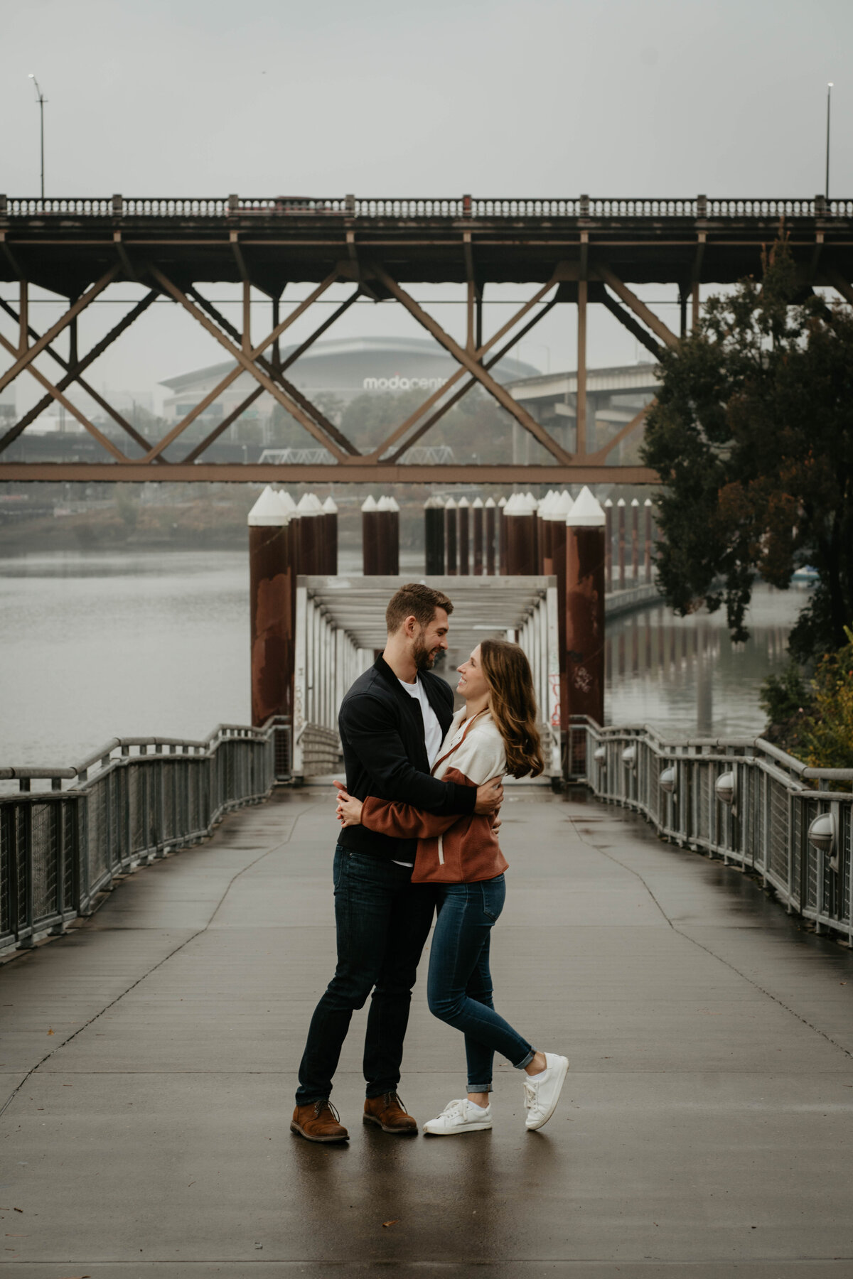 Couple smiling at each other on the Eastbank Esplanade in downtown Portland during engagement photos
