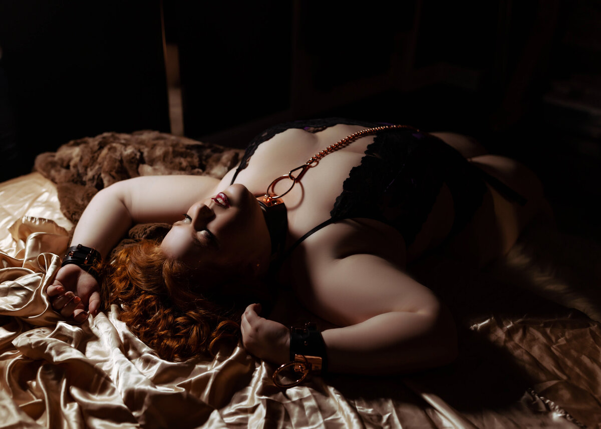 after dark boudoir bondage session with plus size woman laying on gold sheets wearing leash