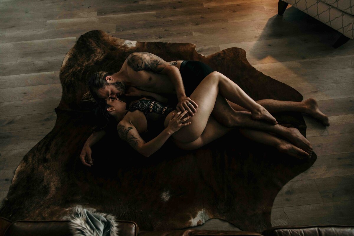 A couple is laying on a rug and embracing each other closely.