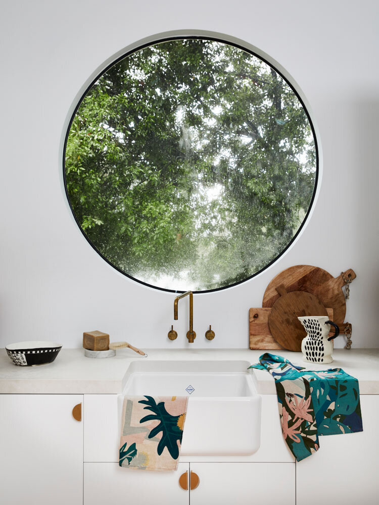 Modern Melbourne kitchen with round window, farmhouse sink, and vibrant linens styled by interior decorator service Melbourne.