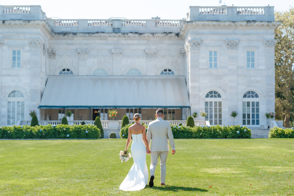 bride and groom walking away with a mansion in the background